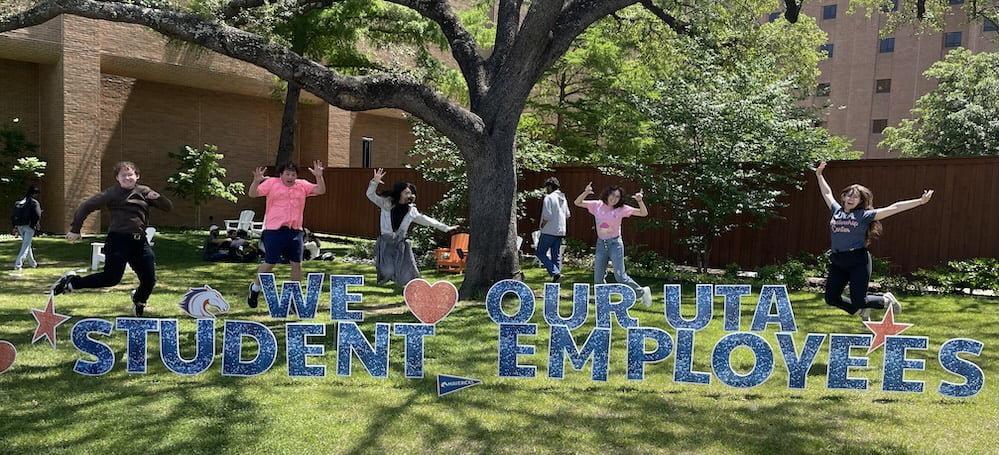 group of people jumping in front of a sign that says we love our uta student employees