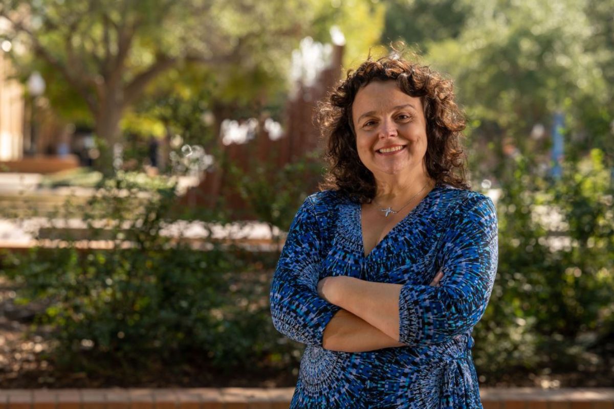 photograph of a female professor smiling in a blue shirt and standing with her arms crossed