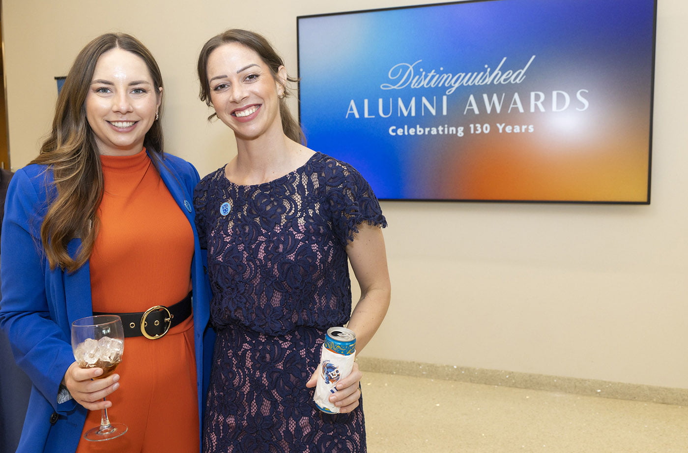 two alumni staff posing in front of the alumni awards sign