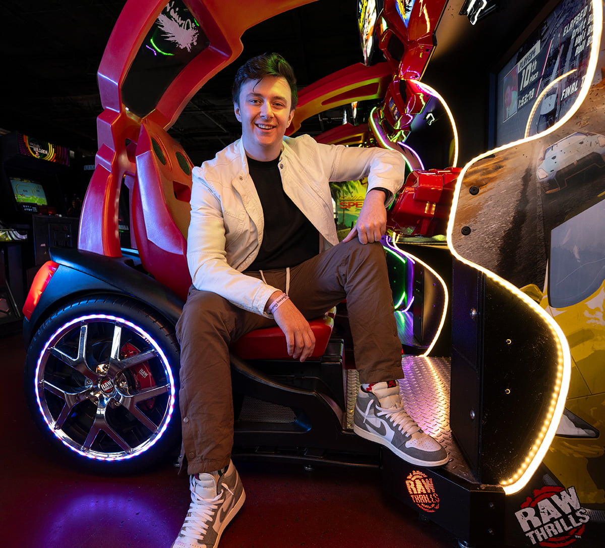 A young man sitting in a video game drivers seat