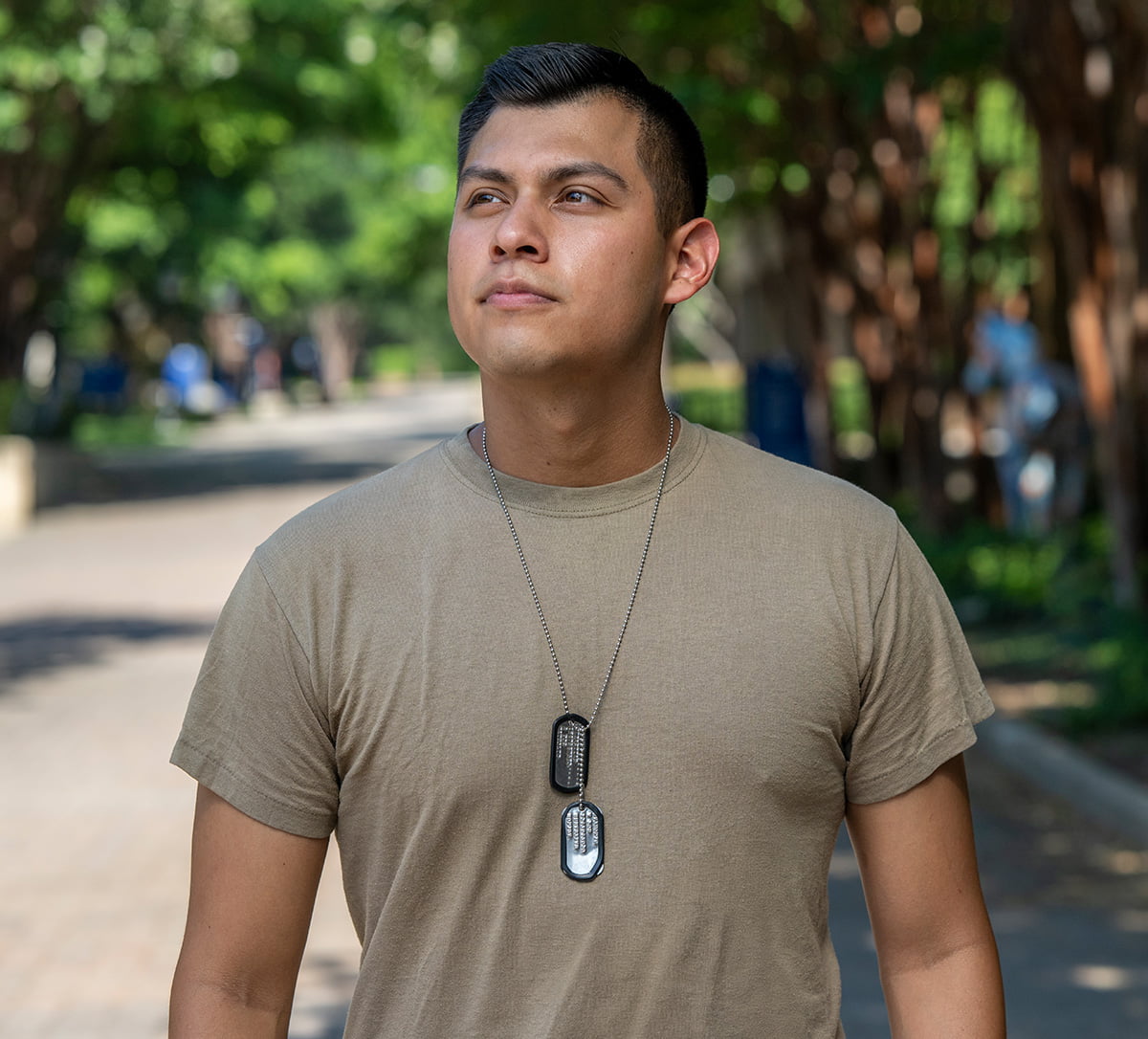 a young man wearing dog tags walking through a college campus
