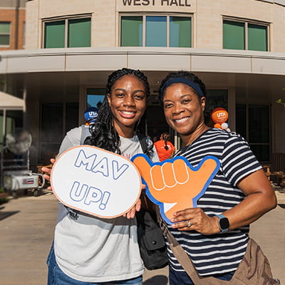 a parent and student pose in front of a dorm