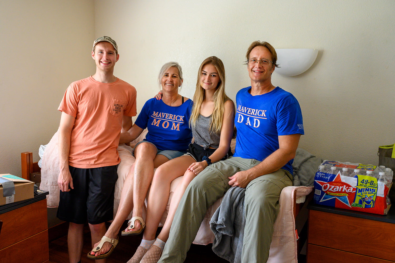 a family of four sitting on a dormitory bed