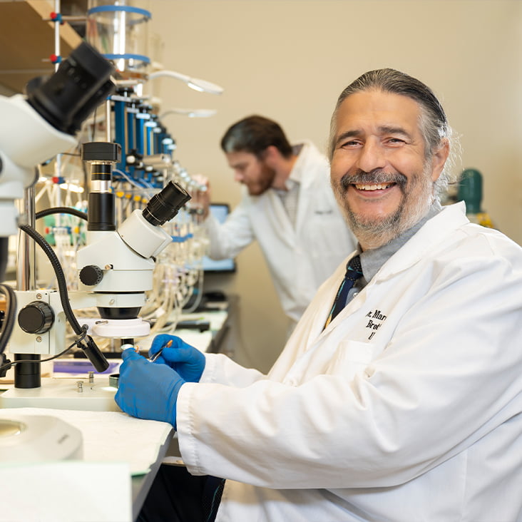 a smiling man sitting at a microscope