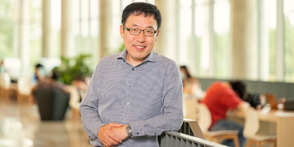 A man stands with his arms folded and smiles for a portrait." _languageinserted="true