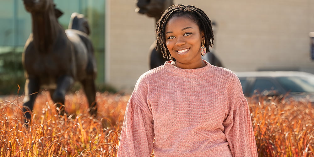 Ariel Hall, graduate student in public health, sits on a concrete wall in front of a UTA building." _languageinserted="true