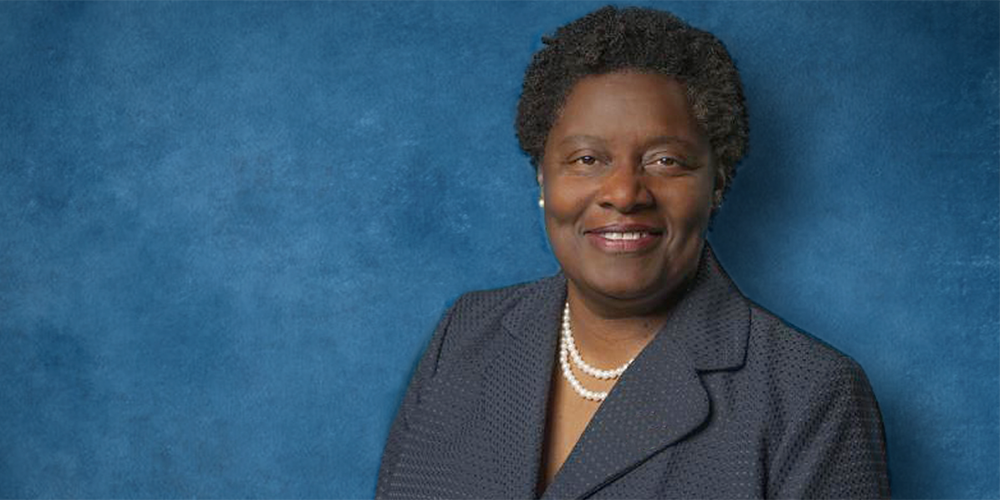 Tamara Brown stands in front of a blue backdrop and smiles for a portrait." _languageinserted="true