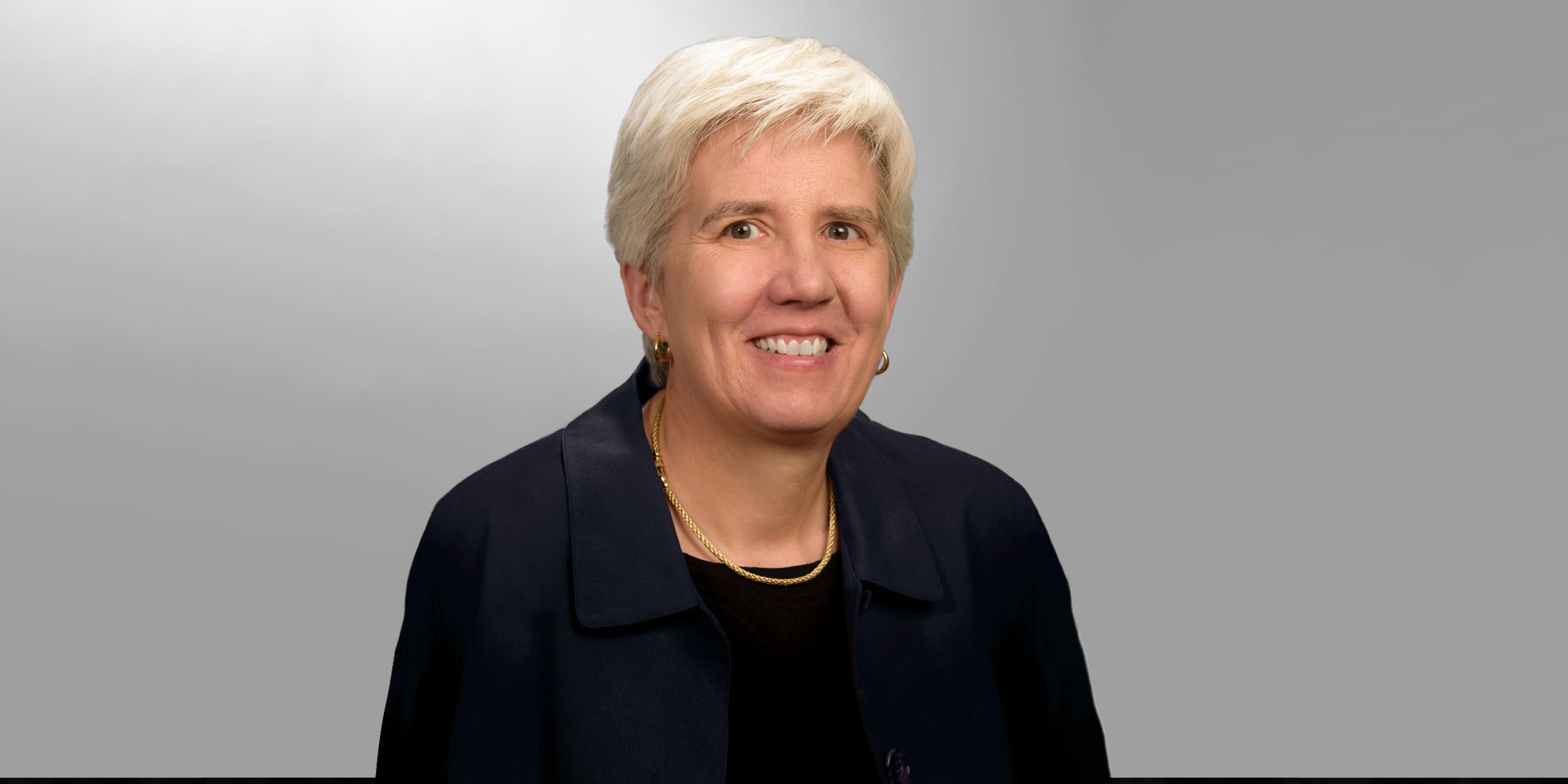 Kate C. Miller smiles for a portrait in front of a gray background. " _languageinserted="true