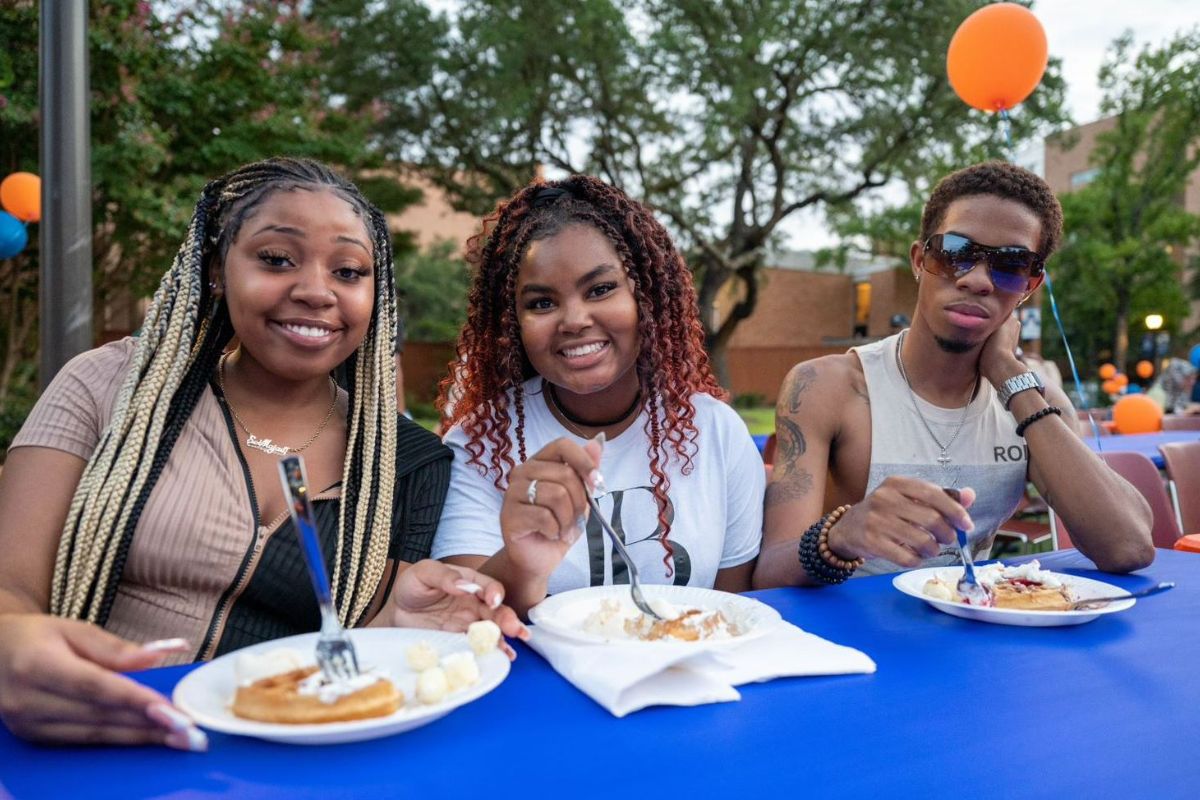 Group of three students sit at table and enjoy waffles at 2022 Waffleopolis event" _languageinserted="true