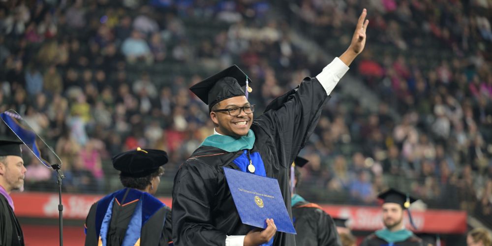 Photo of student dressed in commencement cap and gown waving