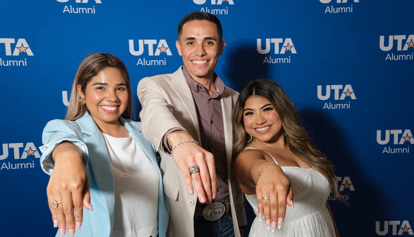 three alumni showing their class rings in front of a background that says u t a alumni