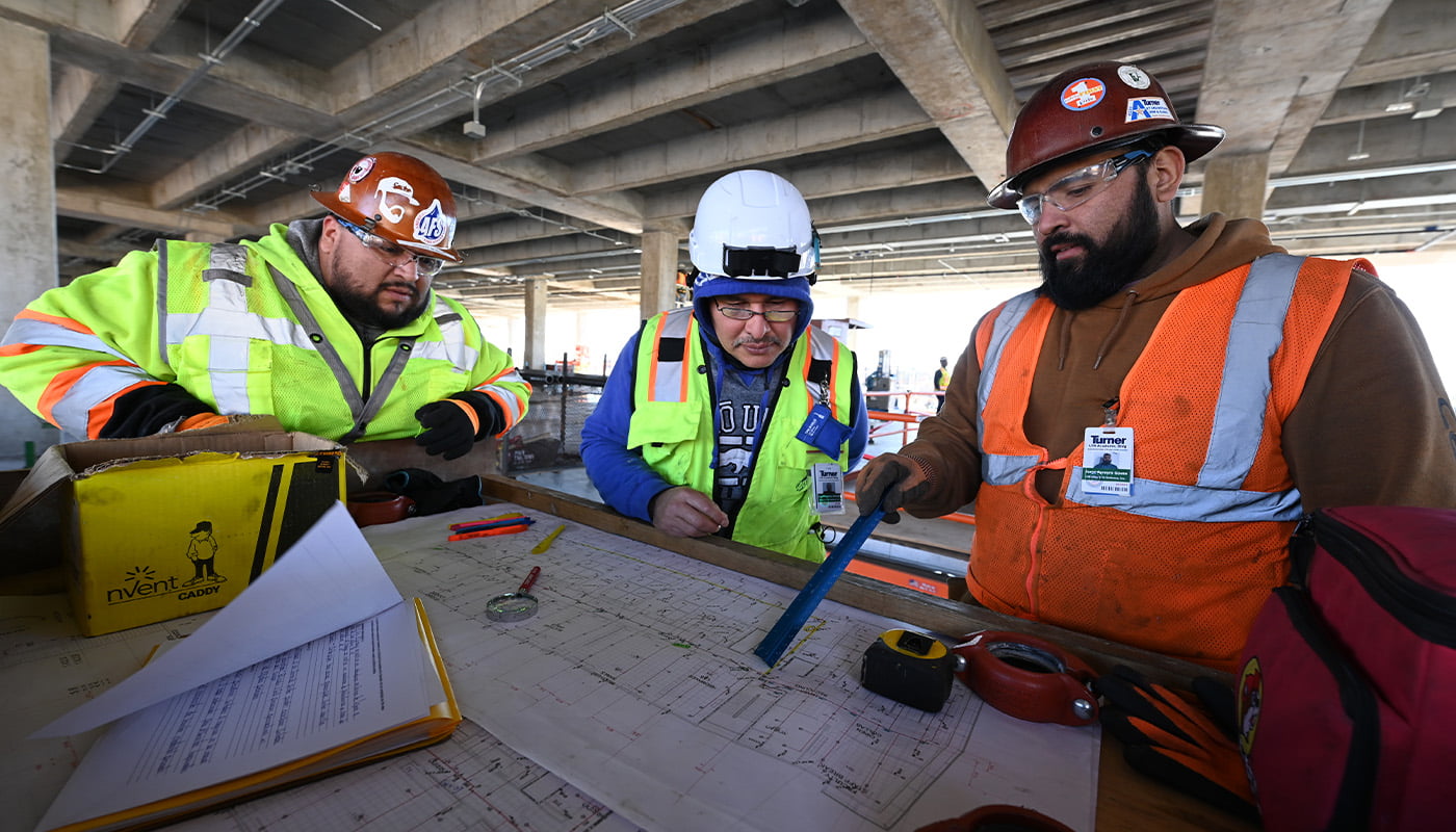 three construction workers pointing to blueprints