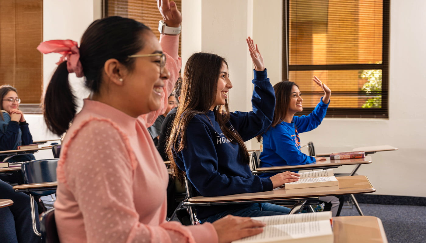 three students in a classroom raising their hands