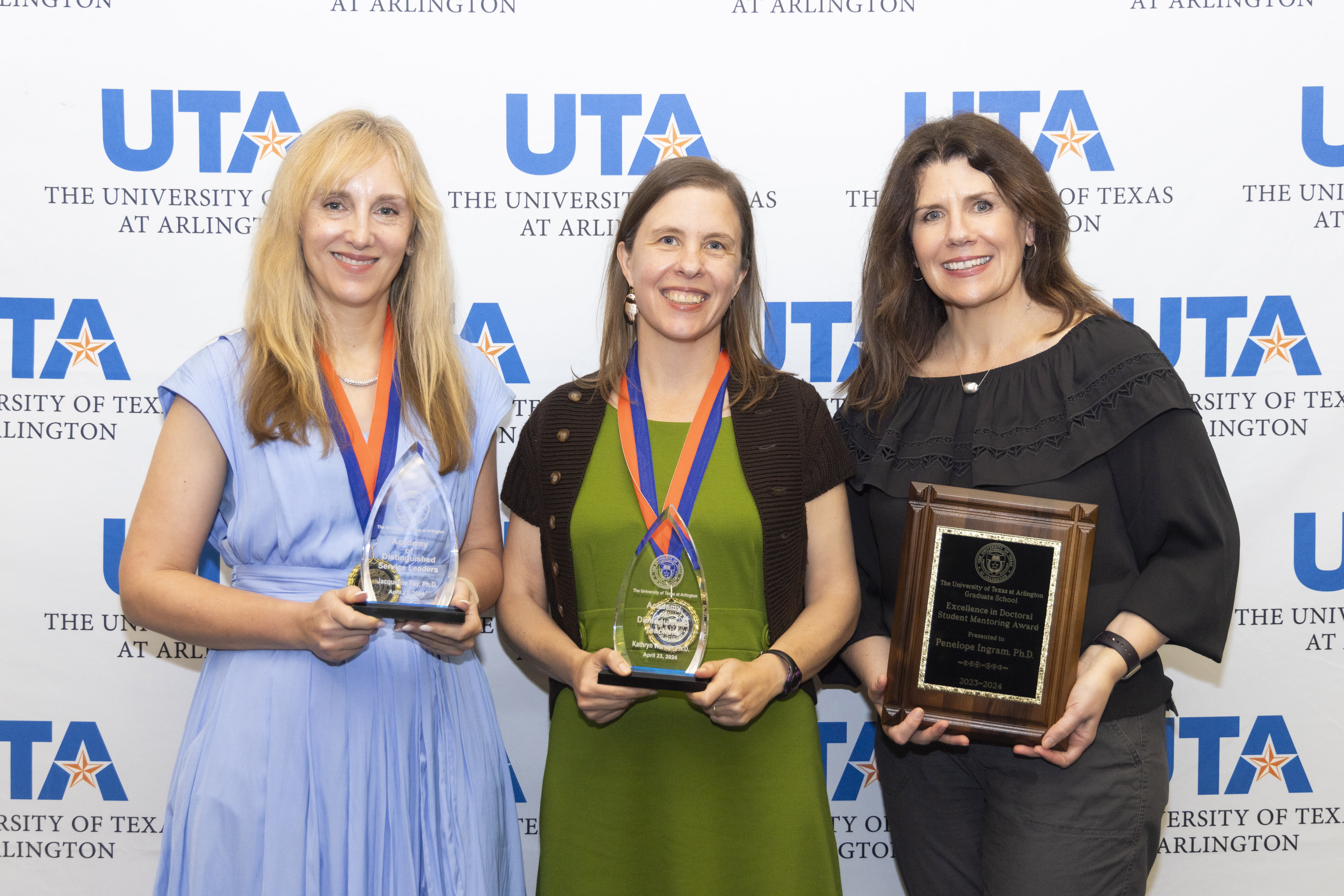 group of 3 people holding awards and standing in front of UTA backdrop