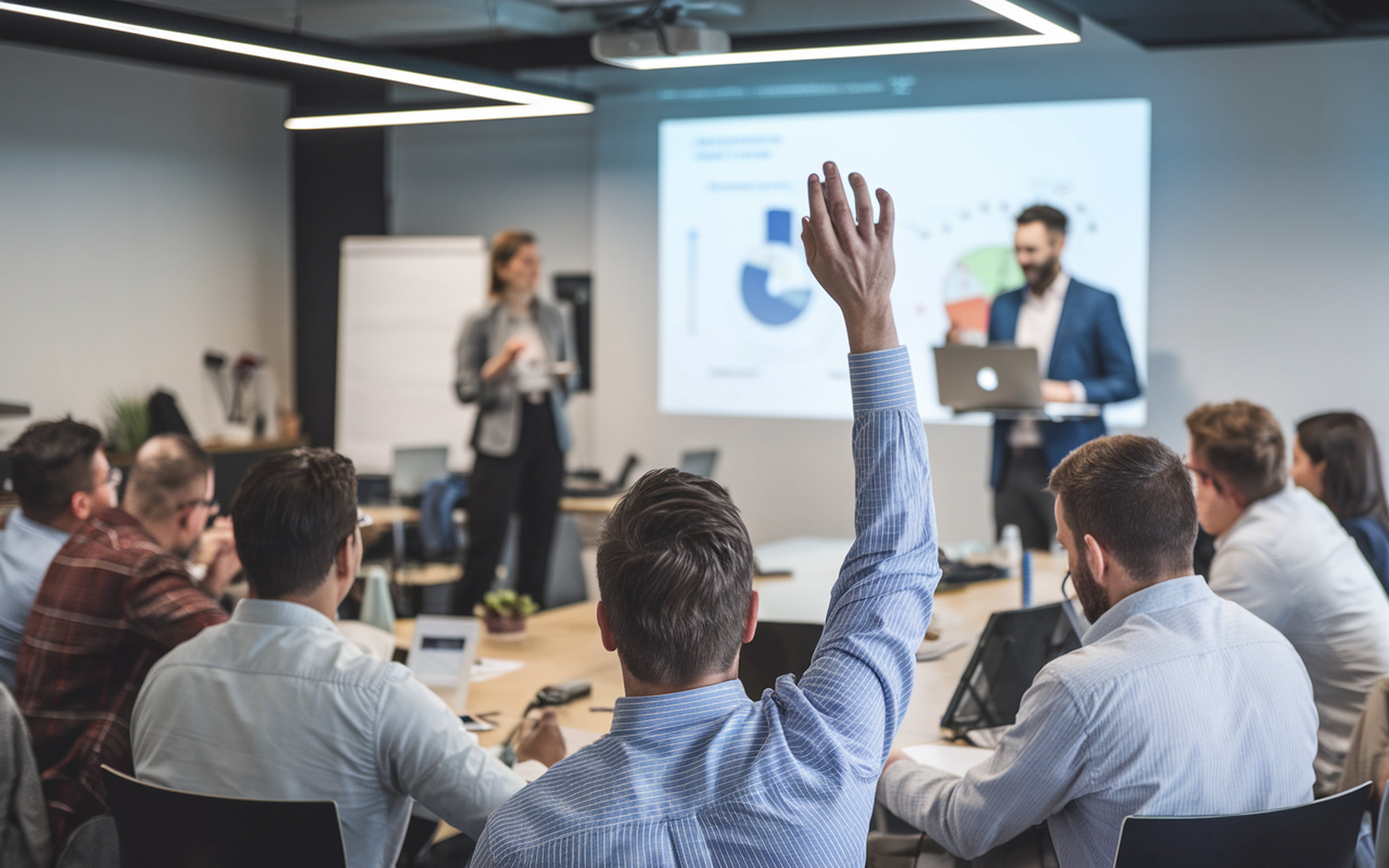 A conference room with a man raising his hand during a presentation.