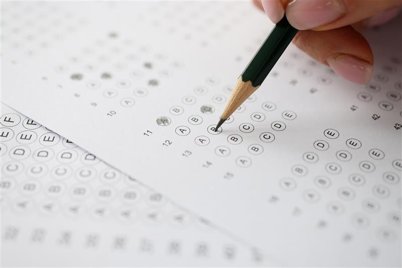 A hand with a pencil fills out a multiple-choice exam sheet, conveying focus and examination.