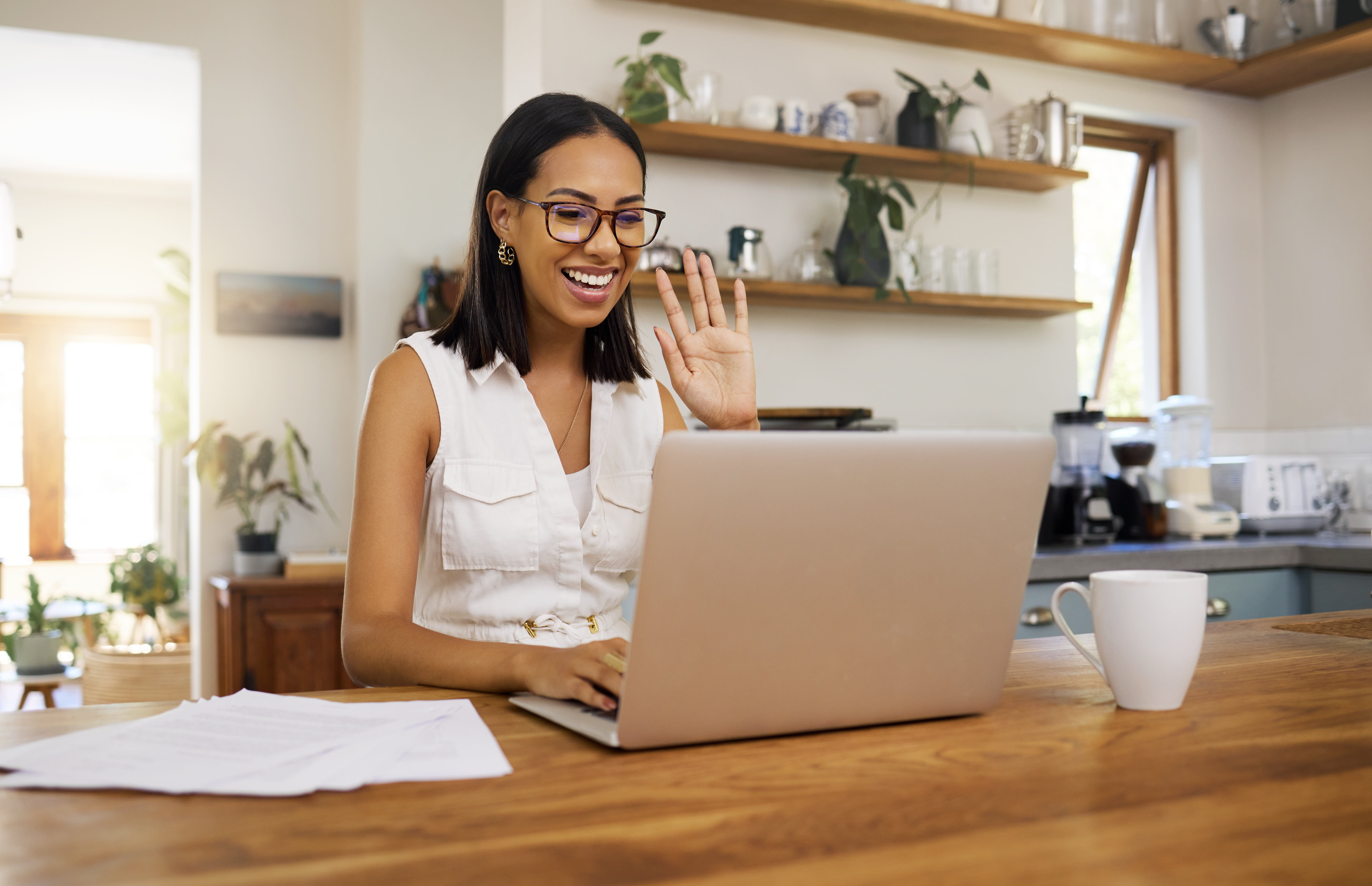 Woman waves during a video call on her laptop