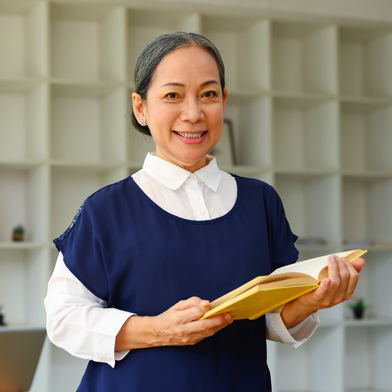 Professor standing in front of shelves with open book in hand