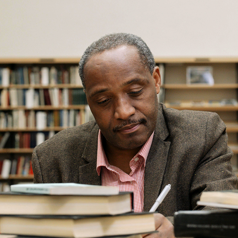 Professor writing on desk with books stacked in foreground