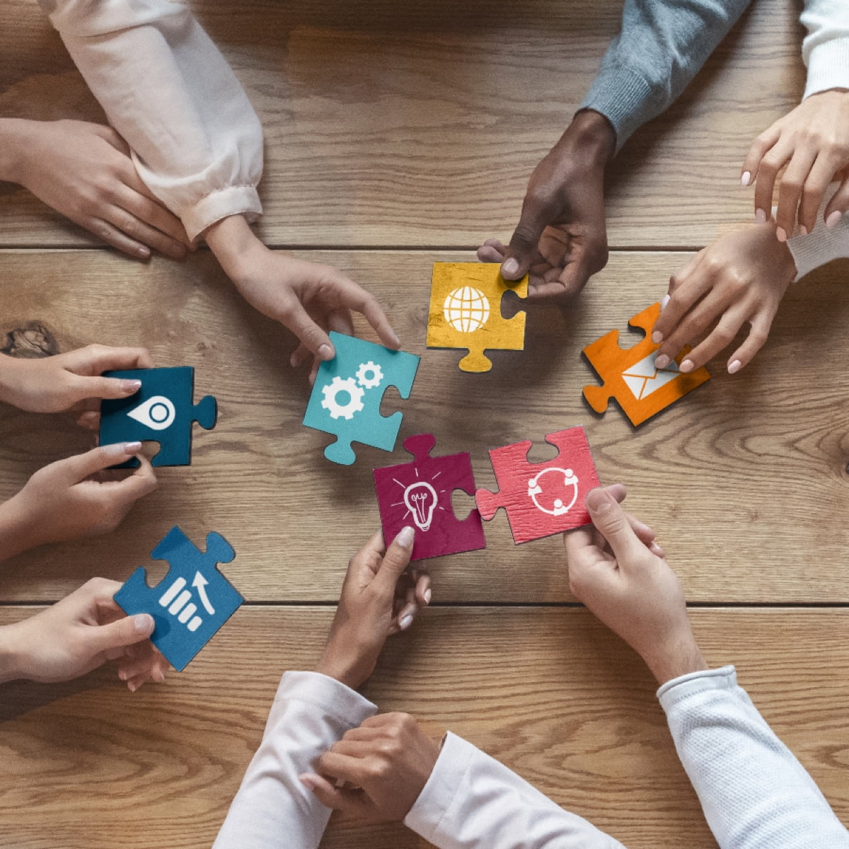 Hands of a diverse team holding colorful puzzle pieces with various collaborative business icons.