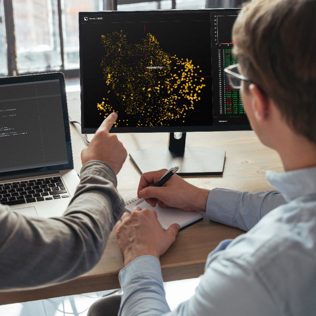 Two researchers analyzing a dense yellow data visualization plot on a computer monitor.