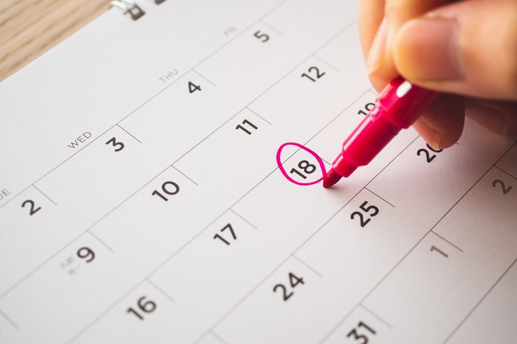 A hand circles the 18th date on a monthly calendar with a pink highlighter, indicating an important event or reminder.