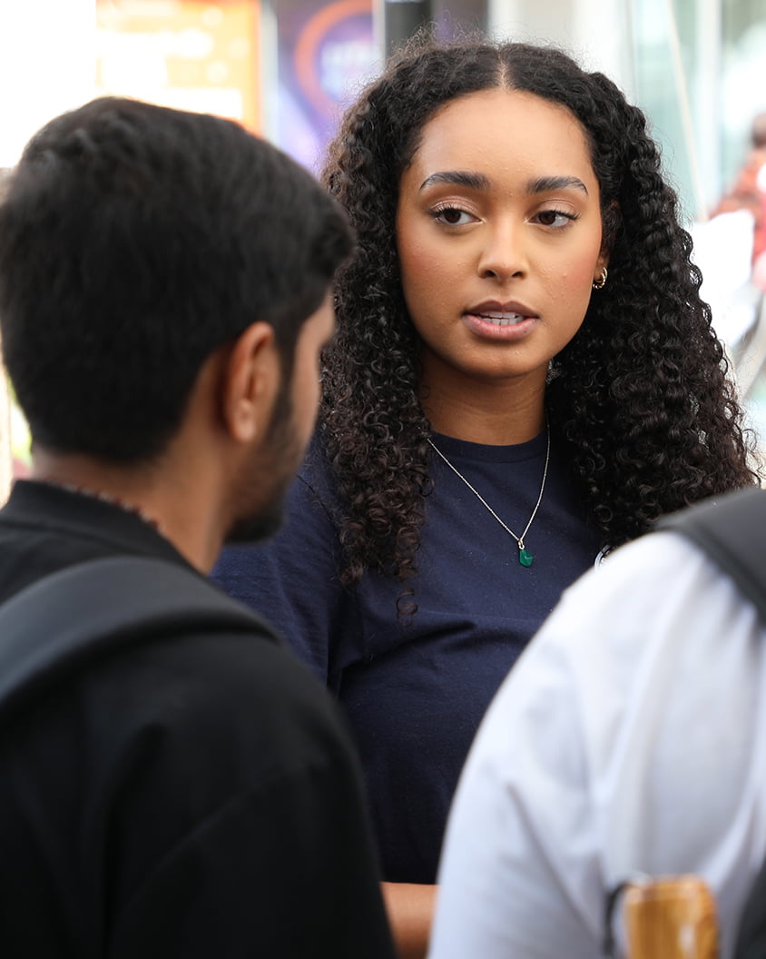 Young female student with curly hair speaks seriously to two men, conveying focused conversation and engagement.