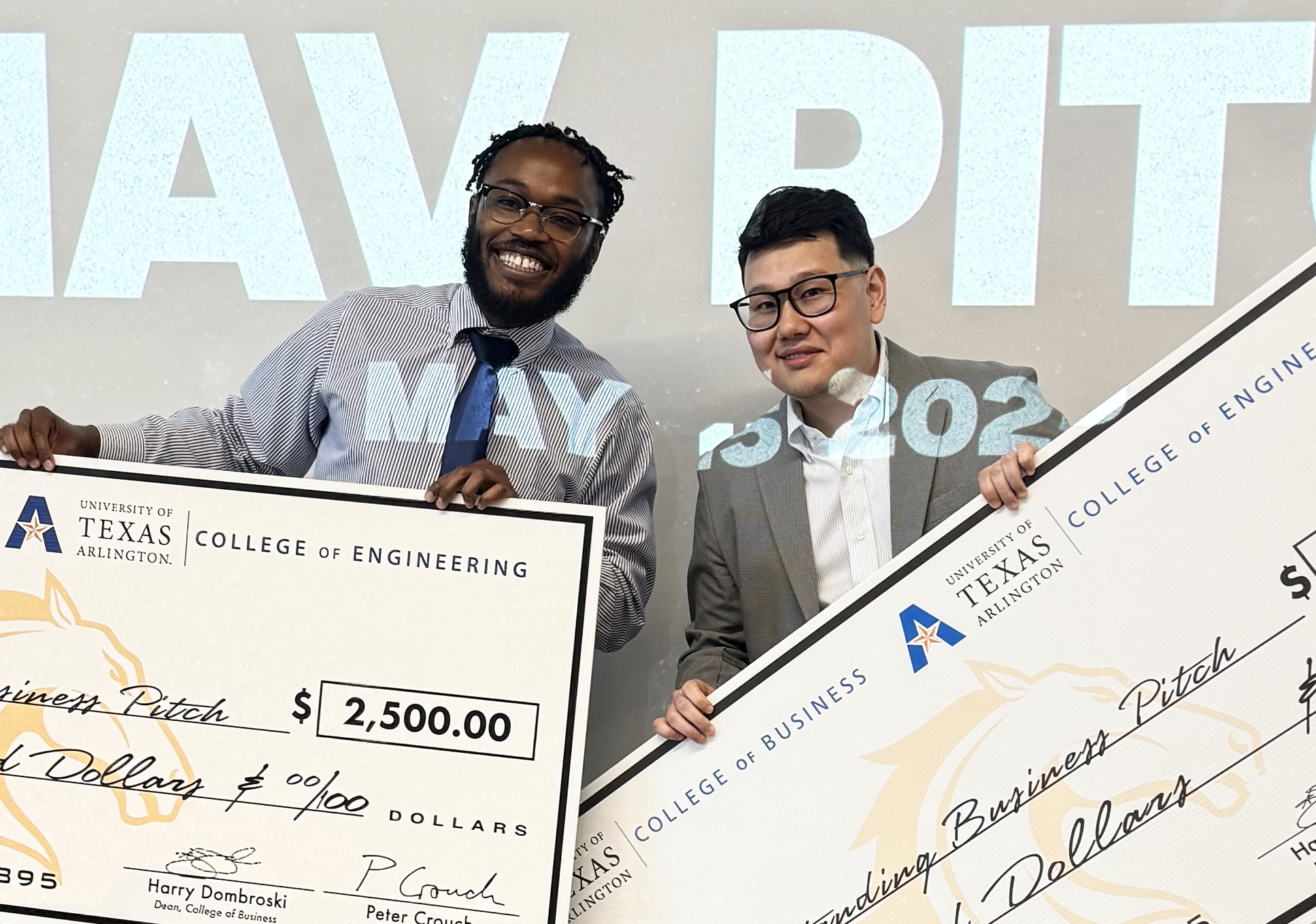 Two individuals hold oversized novelty checks for $2,500 from the University of Texas Arlington's engineering and business colleges.
