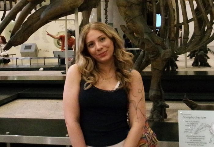 female standing in front of dinosaur skeleton smiling