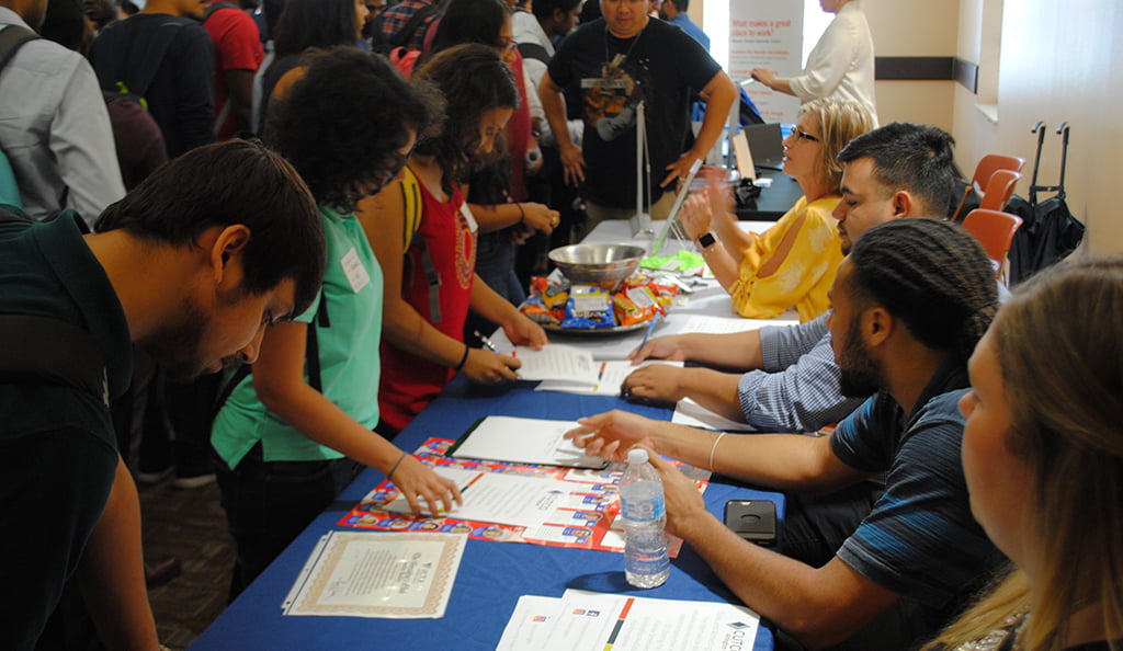 students filling out forms at blue table with people sitting behind table