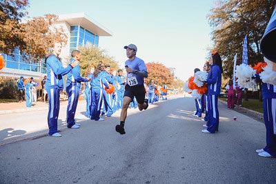 Man running in 5k as he passes by adoring fans on the side.