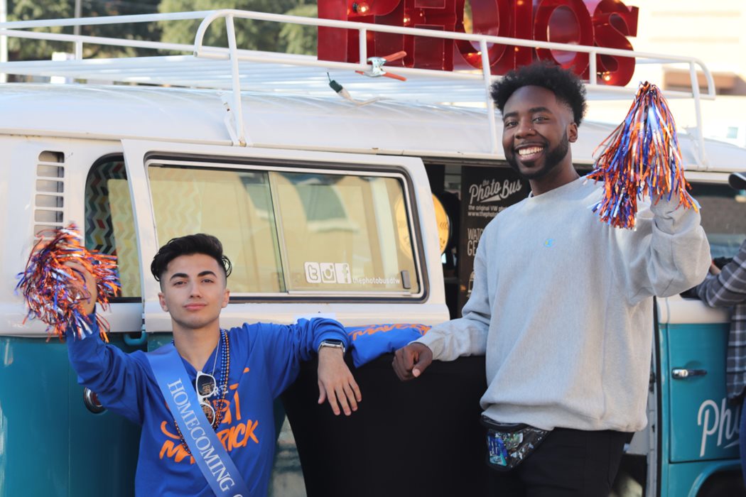 two male students in a white and blue shirt with pompoms in hand