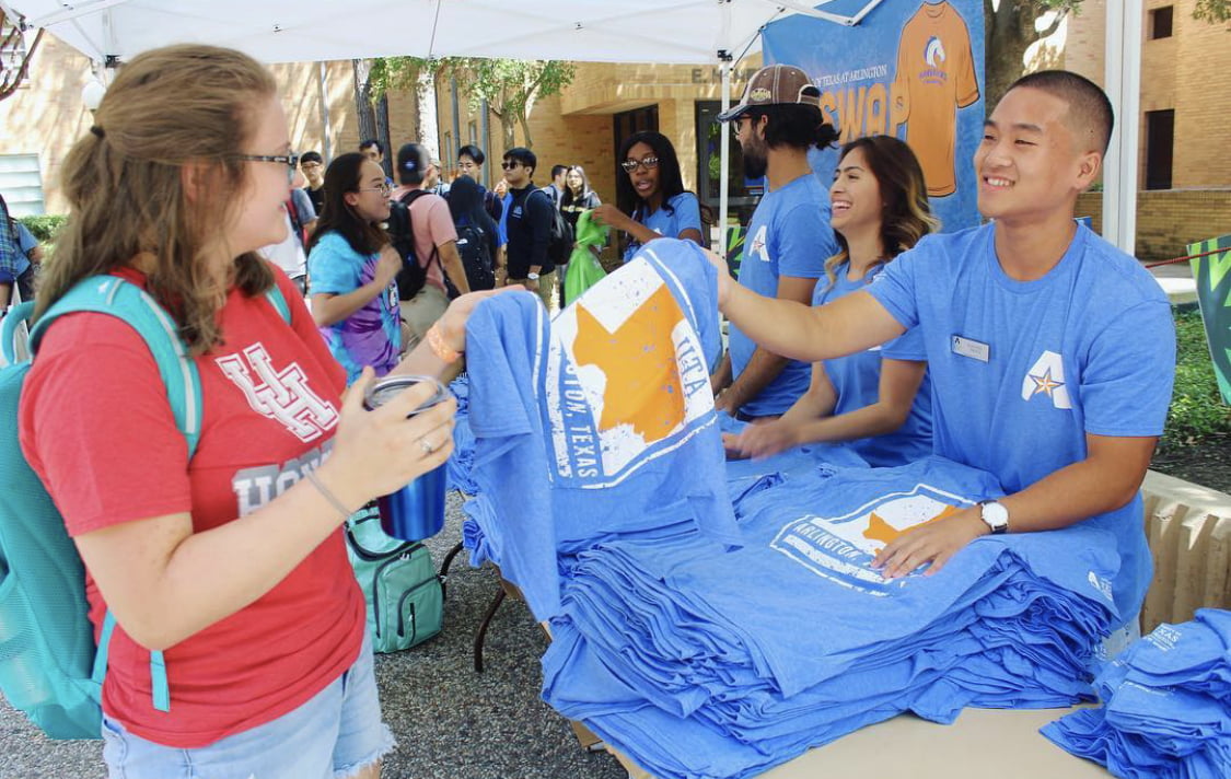 A man handing a T shirt to a woman during the MavSwap event.