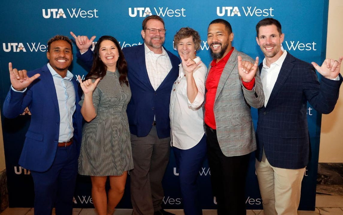 group posing in front of u t a west banner